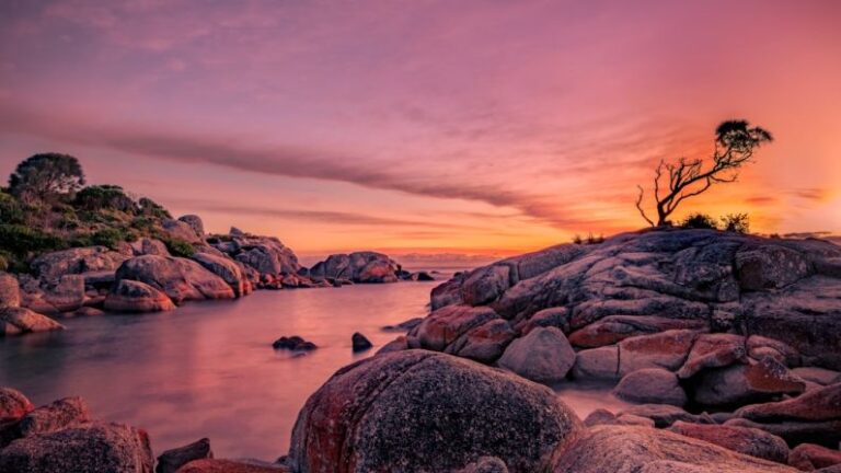 Tasmania - silhouette of person standing on rock formation near body of water during sunset